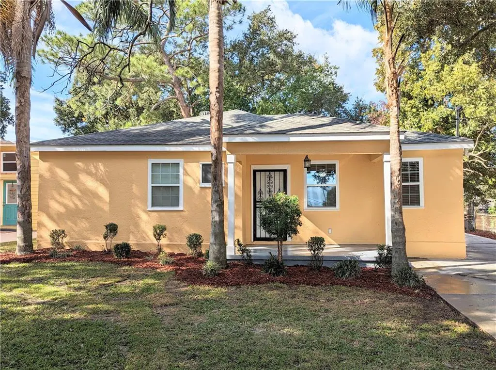 A yellow single-story house with a black security door and palm trees in the front yard.