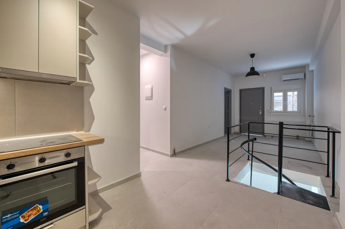 A bright, modern apartment interior with a kitchen area, staircase, and gray door.
