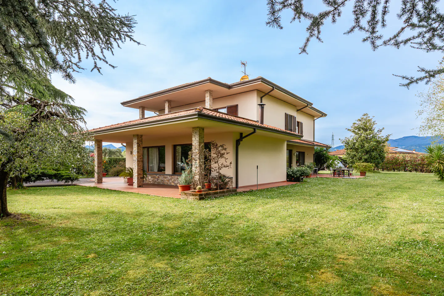 Two-story beige house with a red tile roof and a large green lawn on a sunny day.