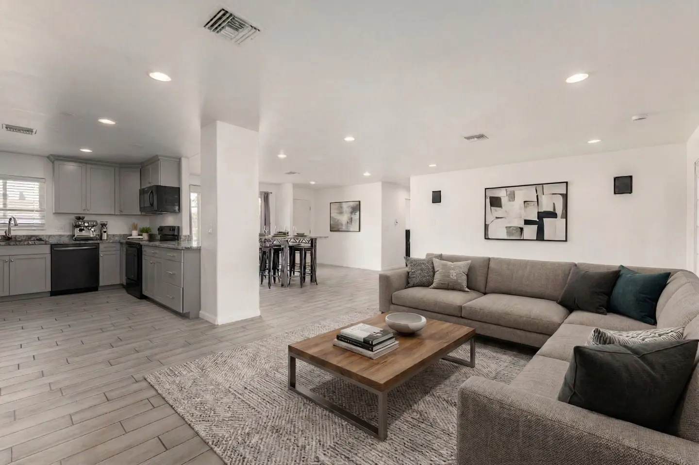 Open-concept living space with gray kitchen cabinets, wood floors, and a large sectional sofa with throw pillows.