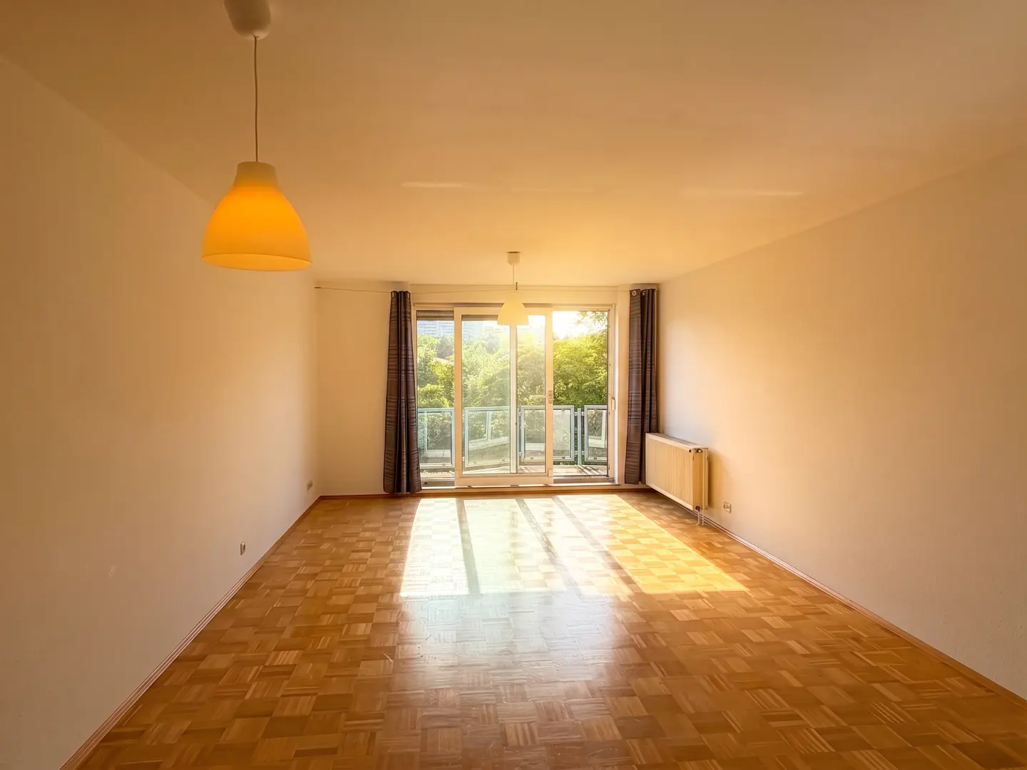 Empty room with light wood parquet flooring, two pendant lights, and a balcony door with sunlight streaming in.