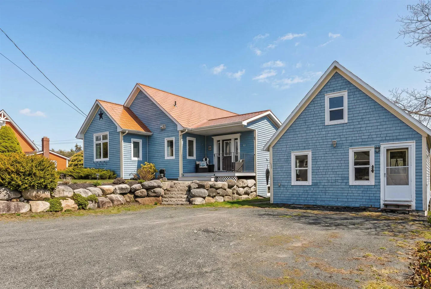 Exterior of a blue house with an orange roof and a stone wall in front of a gravel driveway.