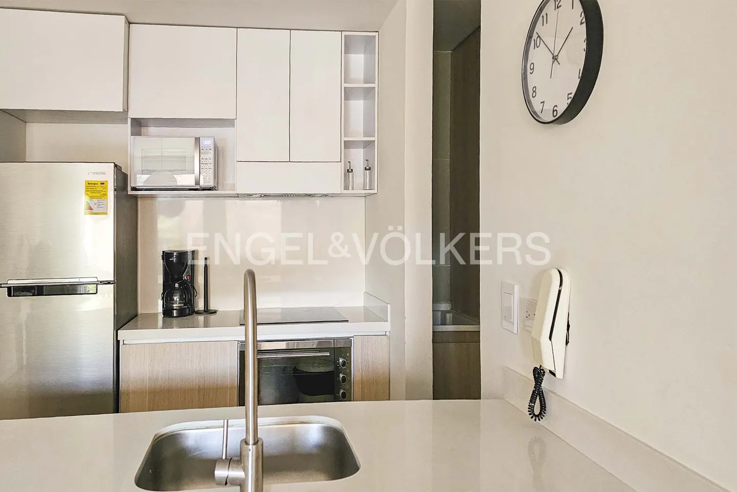 A modern kitchen with white cabinets, stainless steel appliances, and a black clock on the wall.