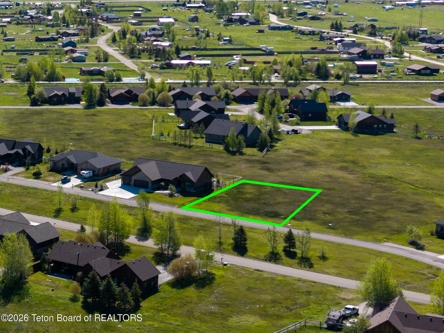 Aerial view of a grassy lot outlined in green, surrounded by houses and trees in a rural neighborhood.