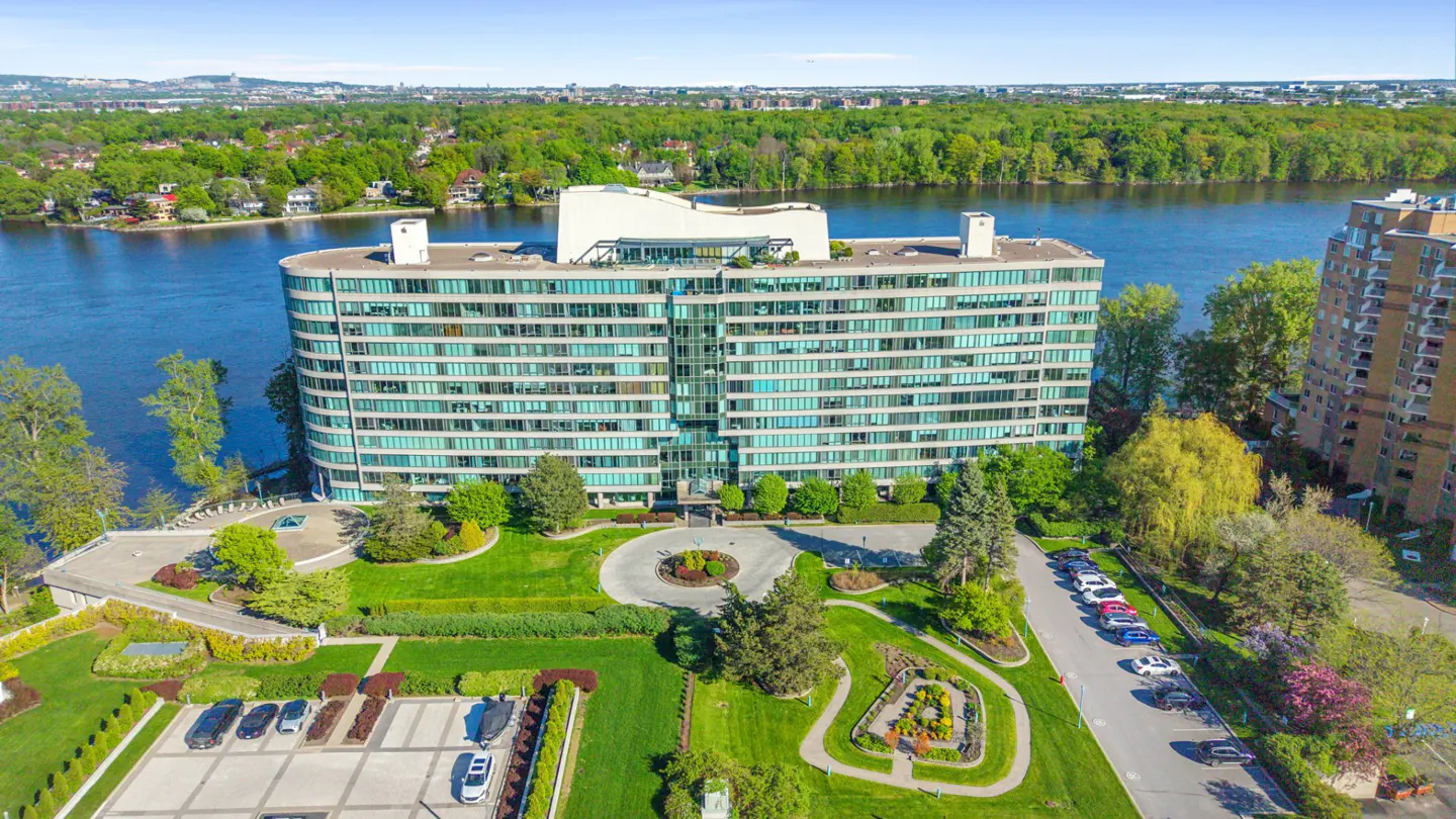 Aerial view of a modern, curved apartment building with a waterfront view and manicured green lawns.