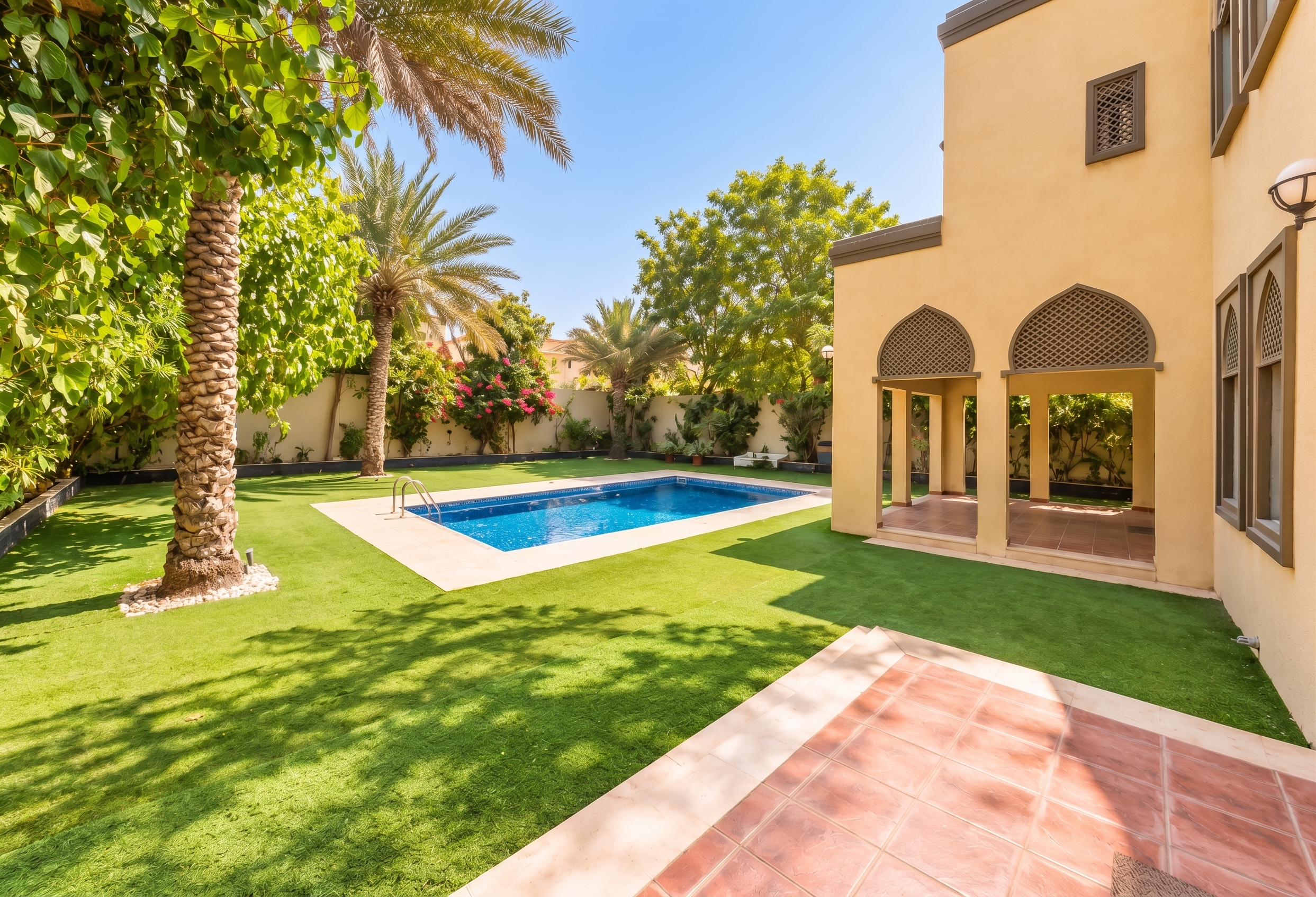 Backyard with a blue swimming pool, green lawn, palm trees, and a beige house with arched covered patio areas. [AI-generated text] [KI-modifiziert]