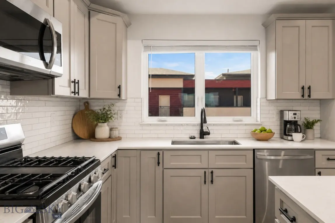 Bright kitchen with gray cabinets, stainless steel appliances, and white subway tile backsplash. A window overlooks nearby buildings.