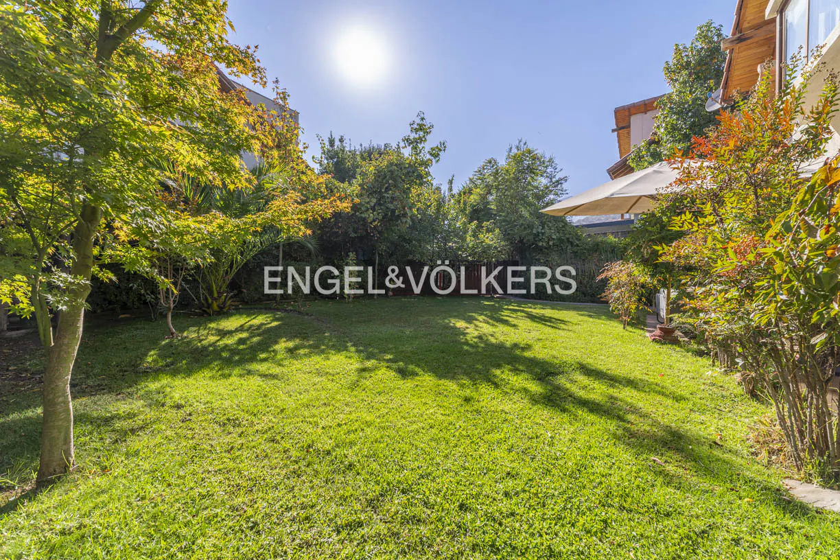 Lush green lawn with trees and the Engel & Völkers logo in the background on a sunny day.