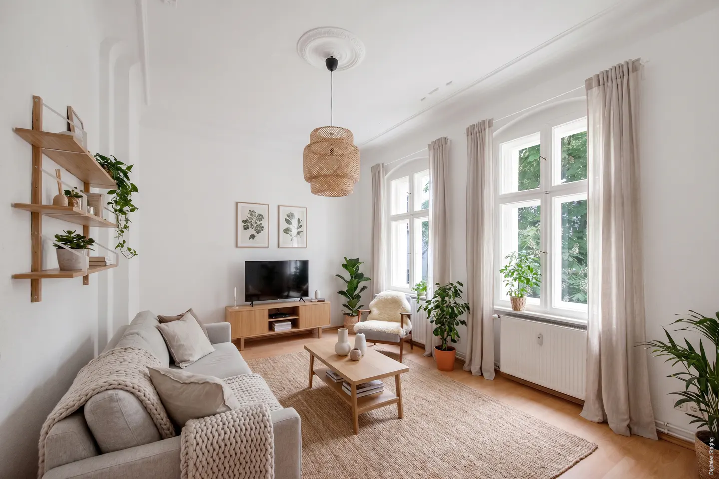 Bright living room with a beige sofa, wooden coffee table, TV console, woven pendant light, and several indoor plants.