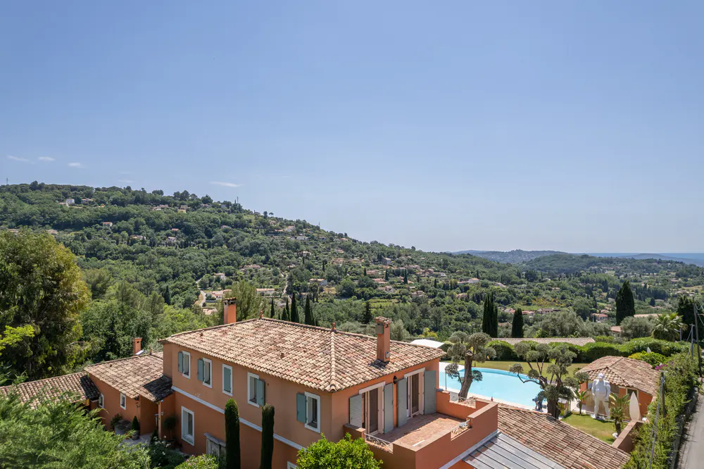 Terracotta-roofed villa with a pool, set against a lush, hilly landscape under a clear blue sky.