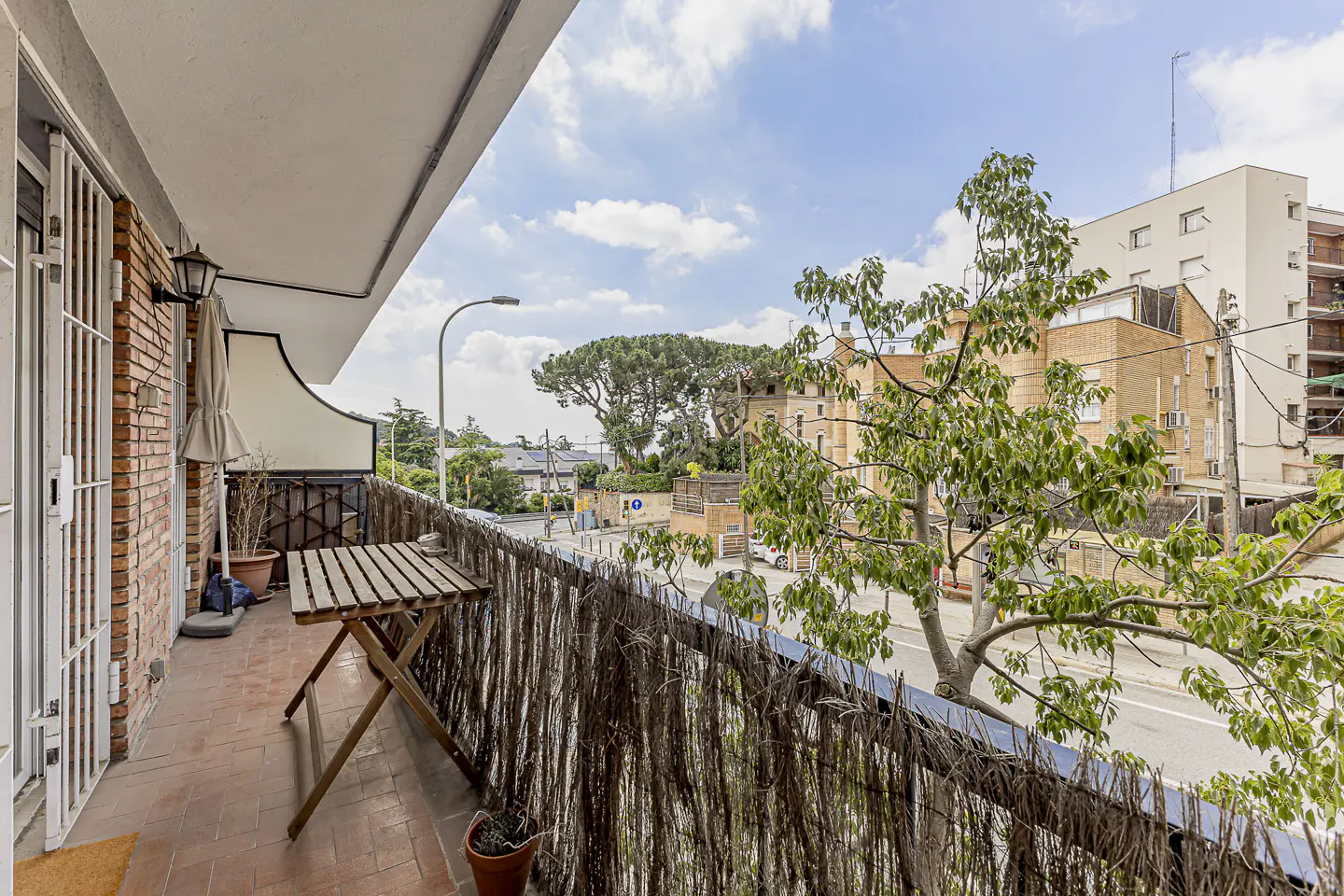 A balcony with a wooden table and a view of a city street with buildings and trees.