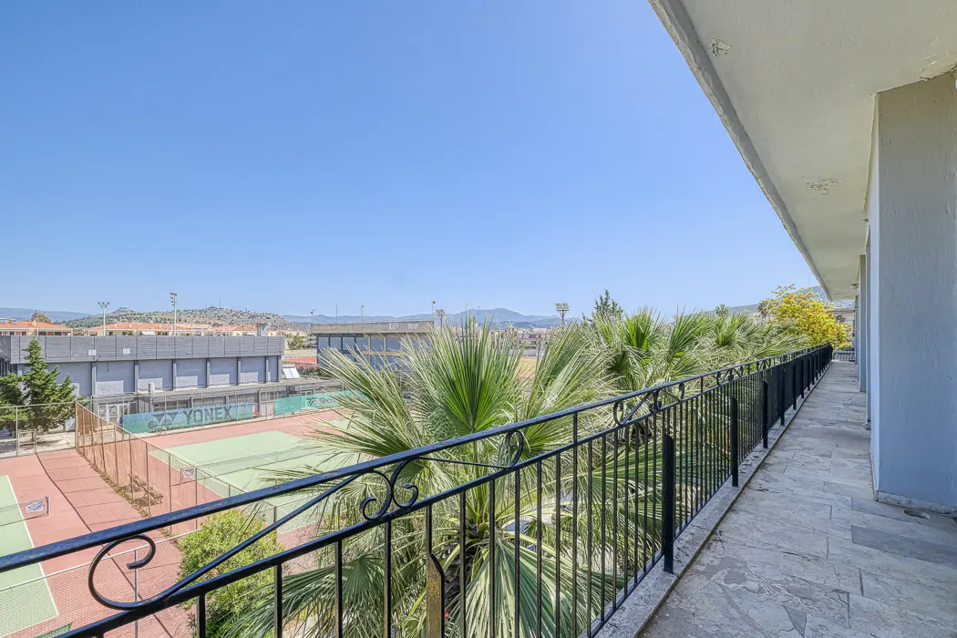 View from a balcony with black iron railings overlooking tennis courts and palm trees on a sunny day.