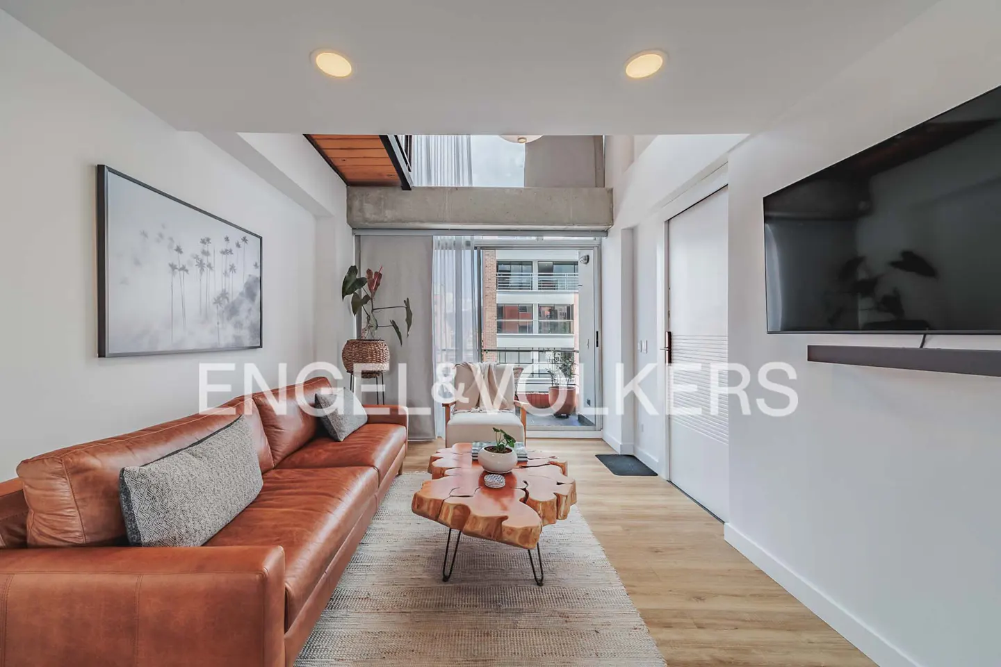 Living room with a brown leather sofa, a wood coffee table, and a balcony with a view of a building.
