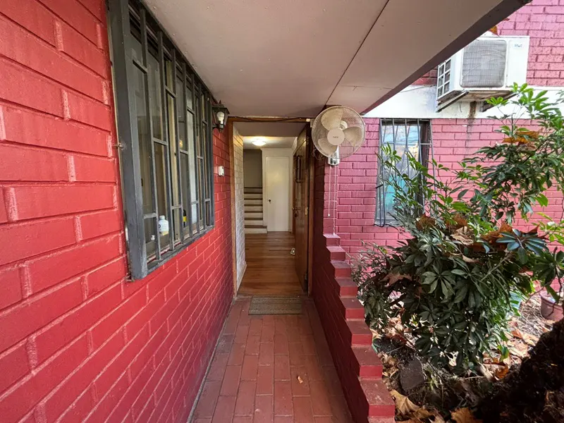 Covered brick entryway with a fan, leading to a door and stairs inside the red brick building.