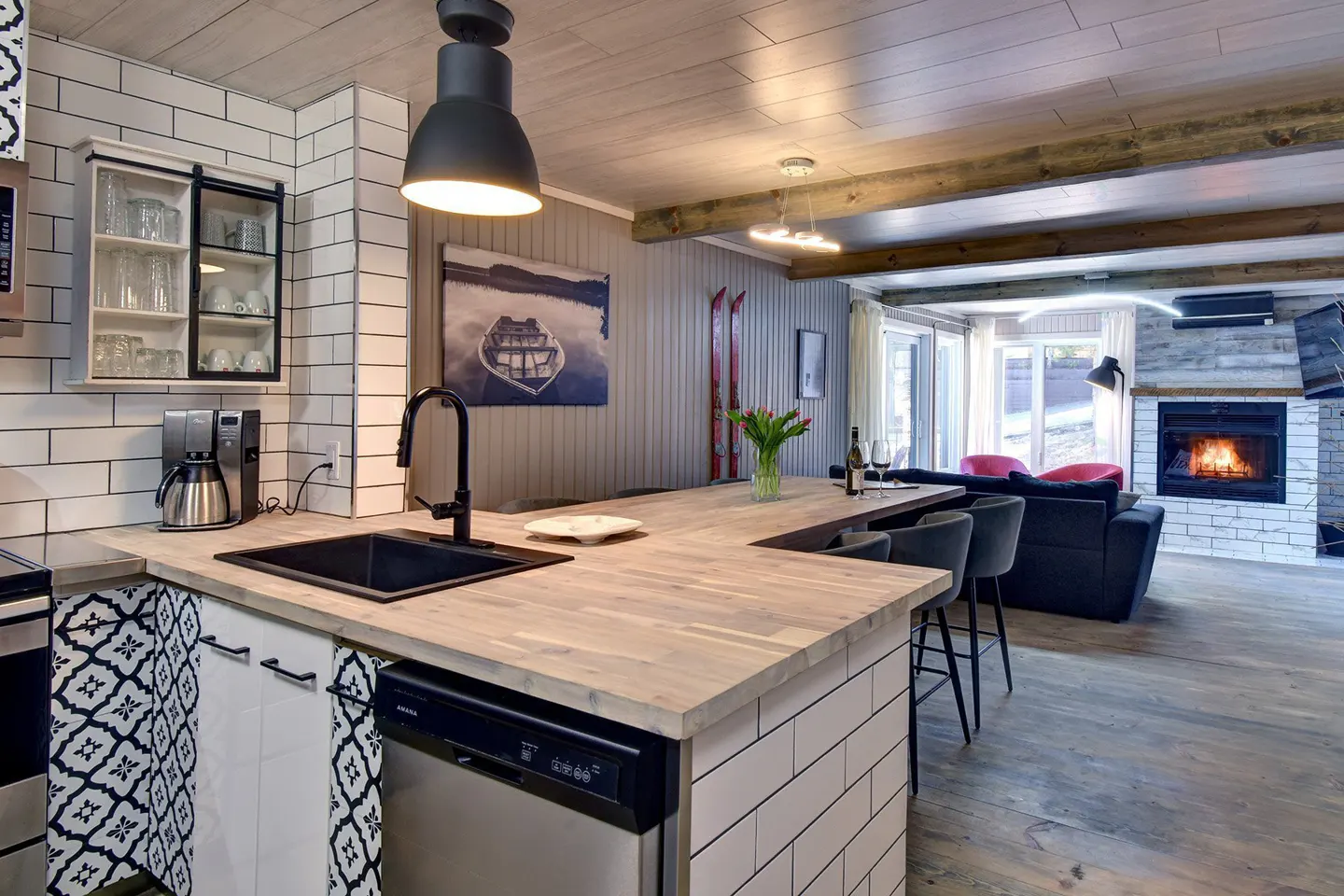 Modern kitchen with wood countertops, black fixtures, and white subway tile, opening into a living room with a fireplace.