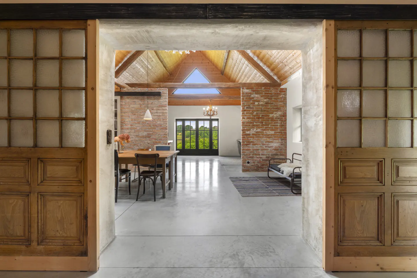Interior view through open wood and glass sliding doors. Dining table, brick wall, and outdoor view visible.