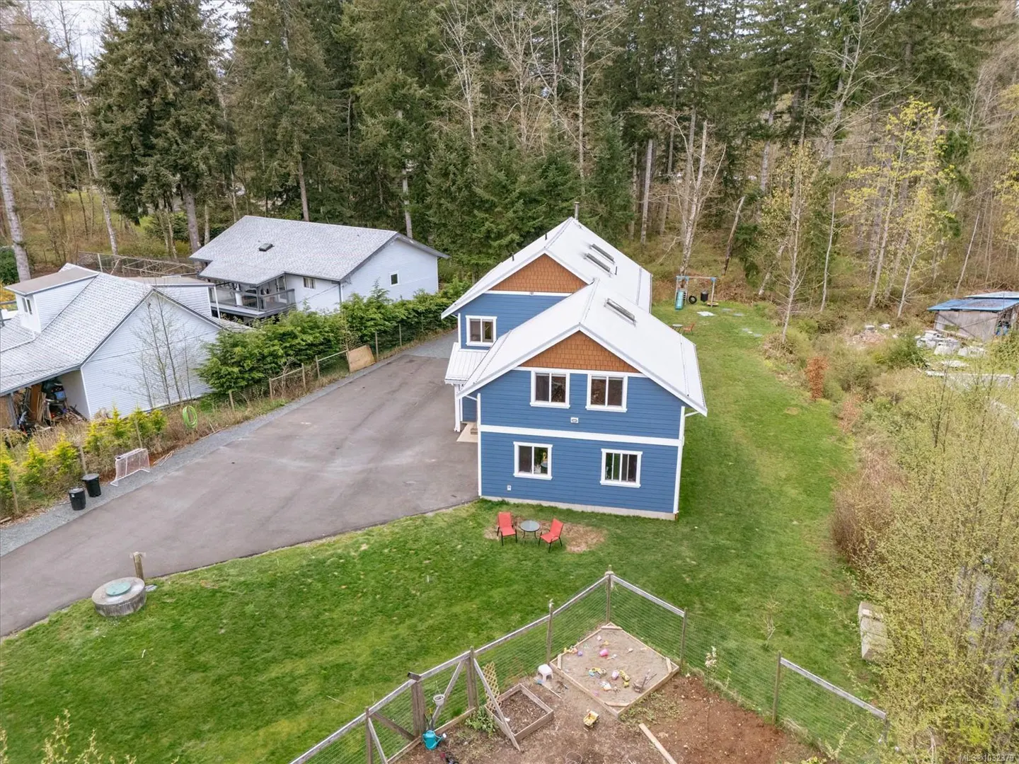Aerial view of a blue two-story house with a white roof, brown trim, and a green lawn with a garden and red chairs.