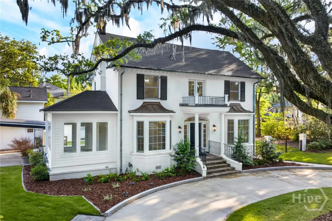Two-story white house with black shutters and a black roof, framed by a large tree with hanging moss.