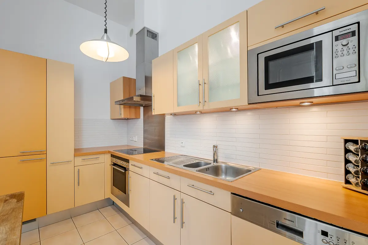 A modern kitchen with light wood cabinets, stainless steel appliances, and white subway tile backsplash. A pendant light hangs above.