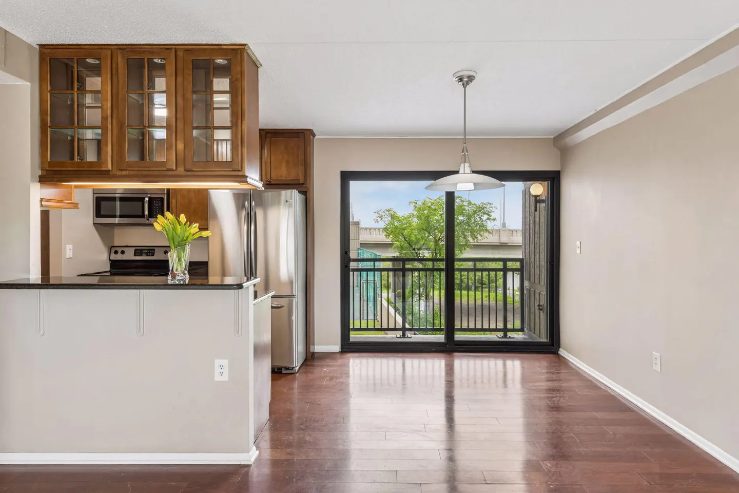 A bright apartment interior with wood floors, a kitchen bar, and a balcony view.