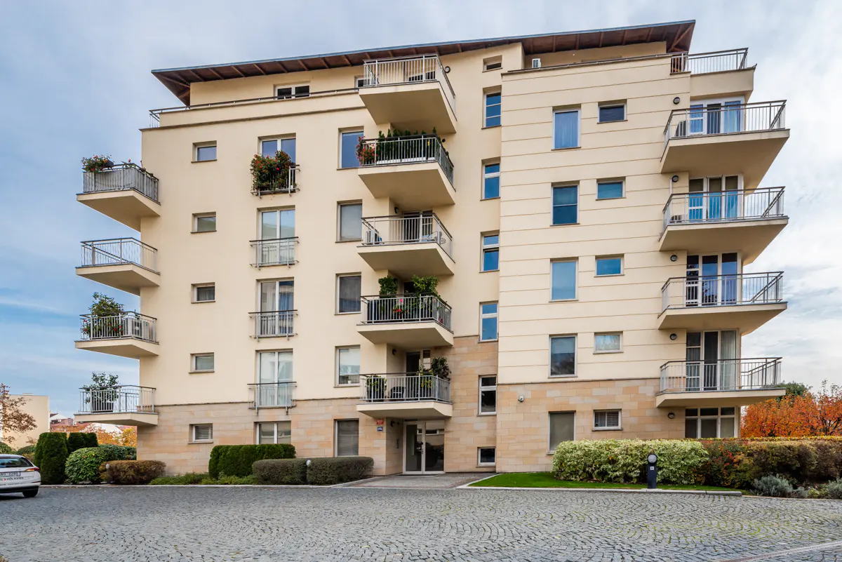 A six-story beige apartment building with balconies and a cobblestone driveway.