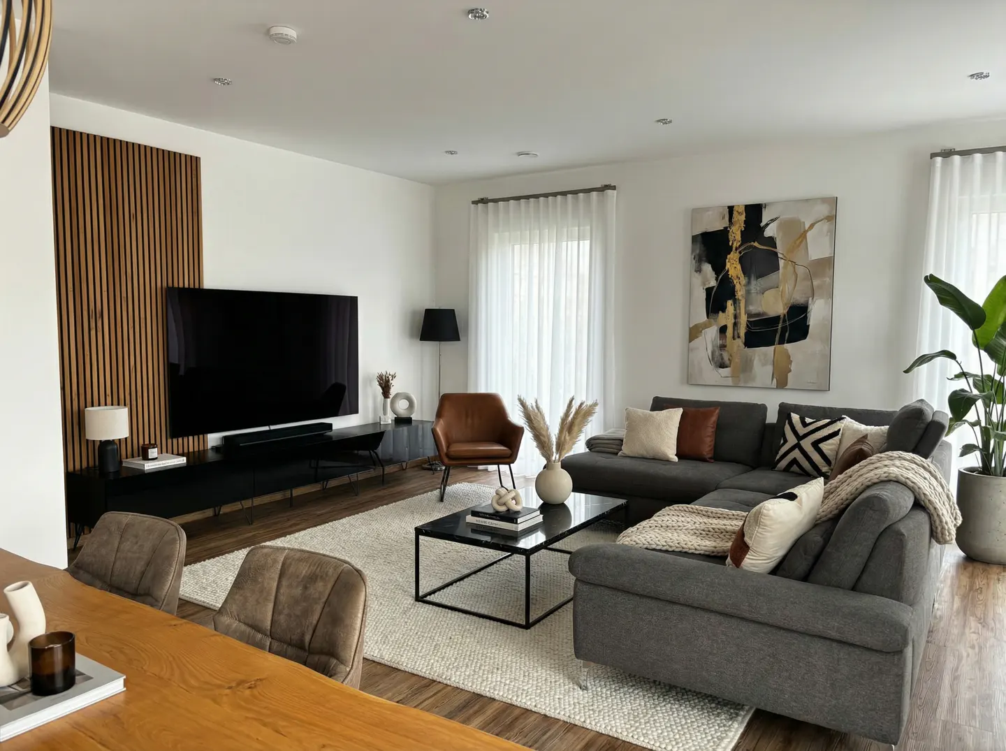 Bright living room with gray sectional sofa, black TV stand with a large TV, and abstract art. A light rug covers the floor.