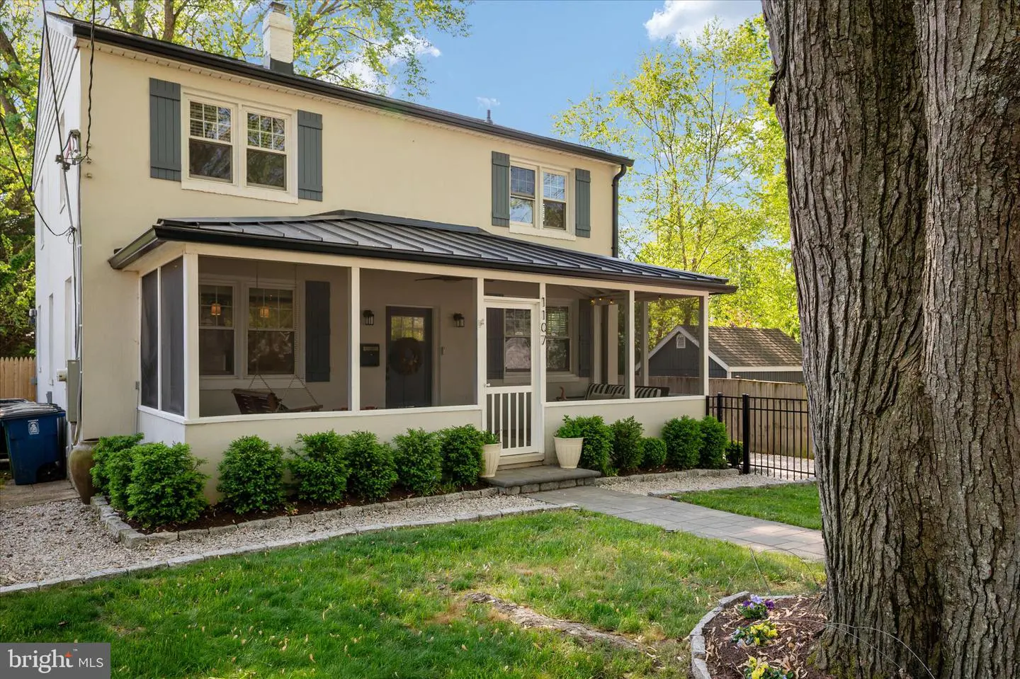Two-story house with a screened-in porch, gray shutters, and a black metal roof. A tree is on the right side of the image.