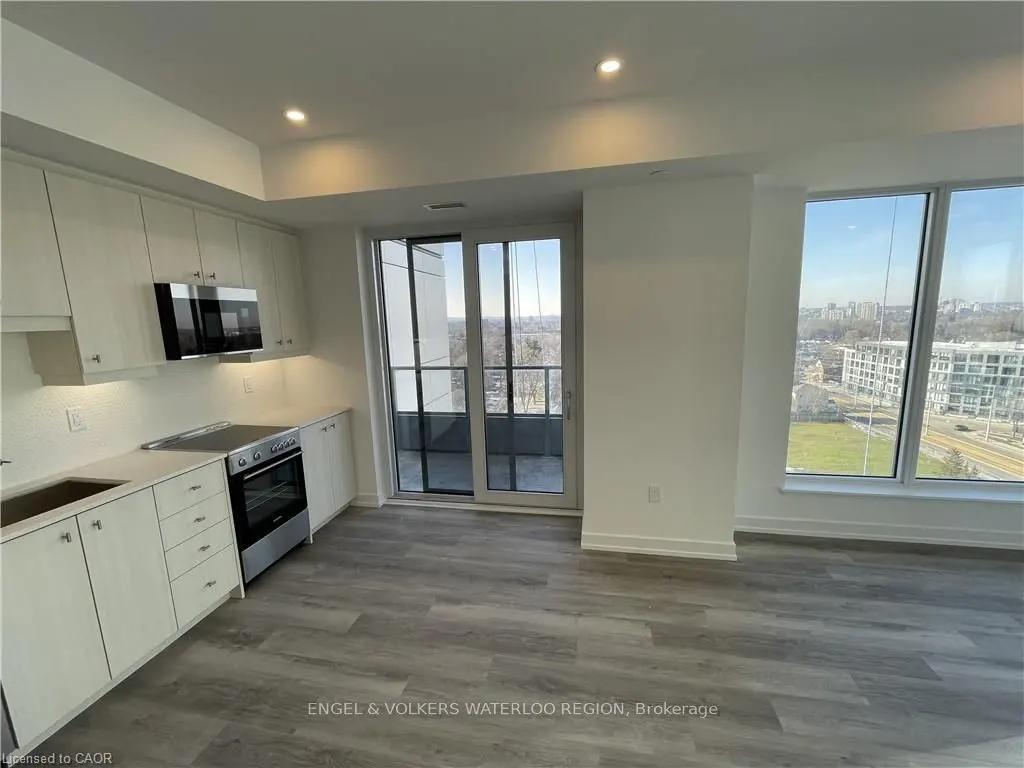 Bright, modern kitchen with white cabinets, stainless steel appliances, and gray wood-look flooring. Sliding glass doors lead to a balcony with a city view.