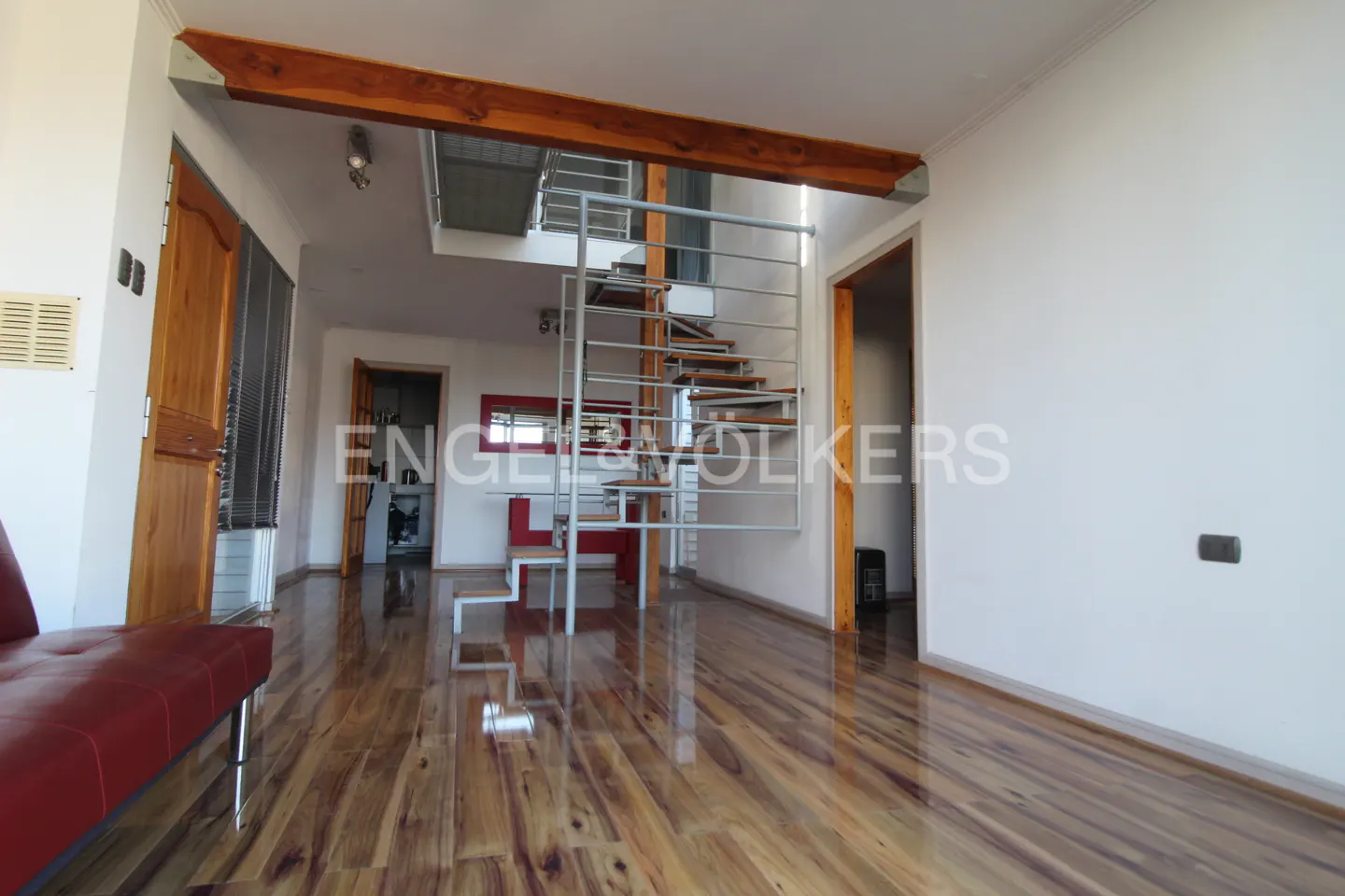 Interior view of a modern home with wood floors, a metal staircase, and a red sofa.