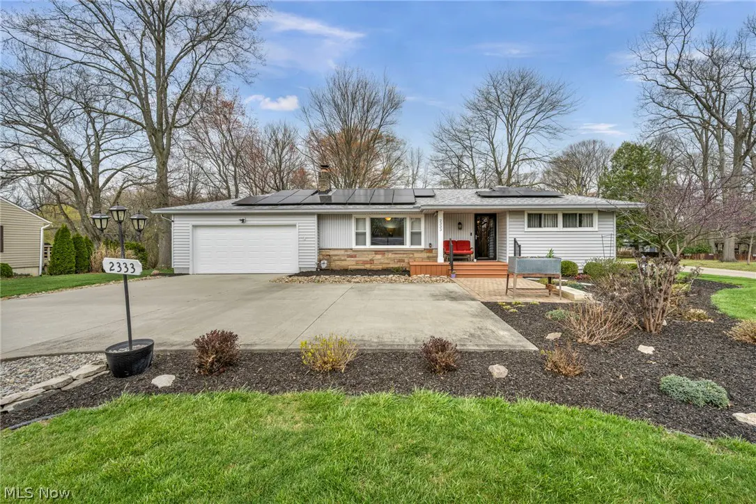 Front exterior of a one-story, light gray house with solar panels, a white garage door, and a concrete driveway.