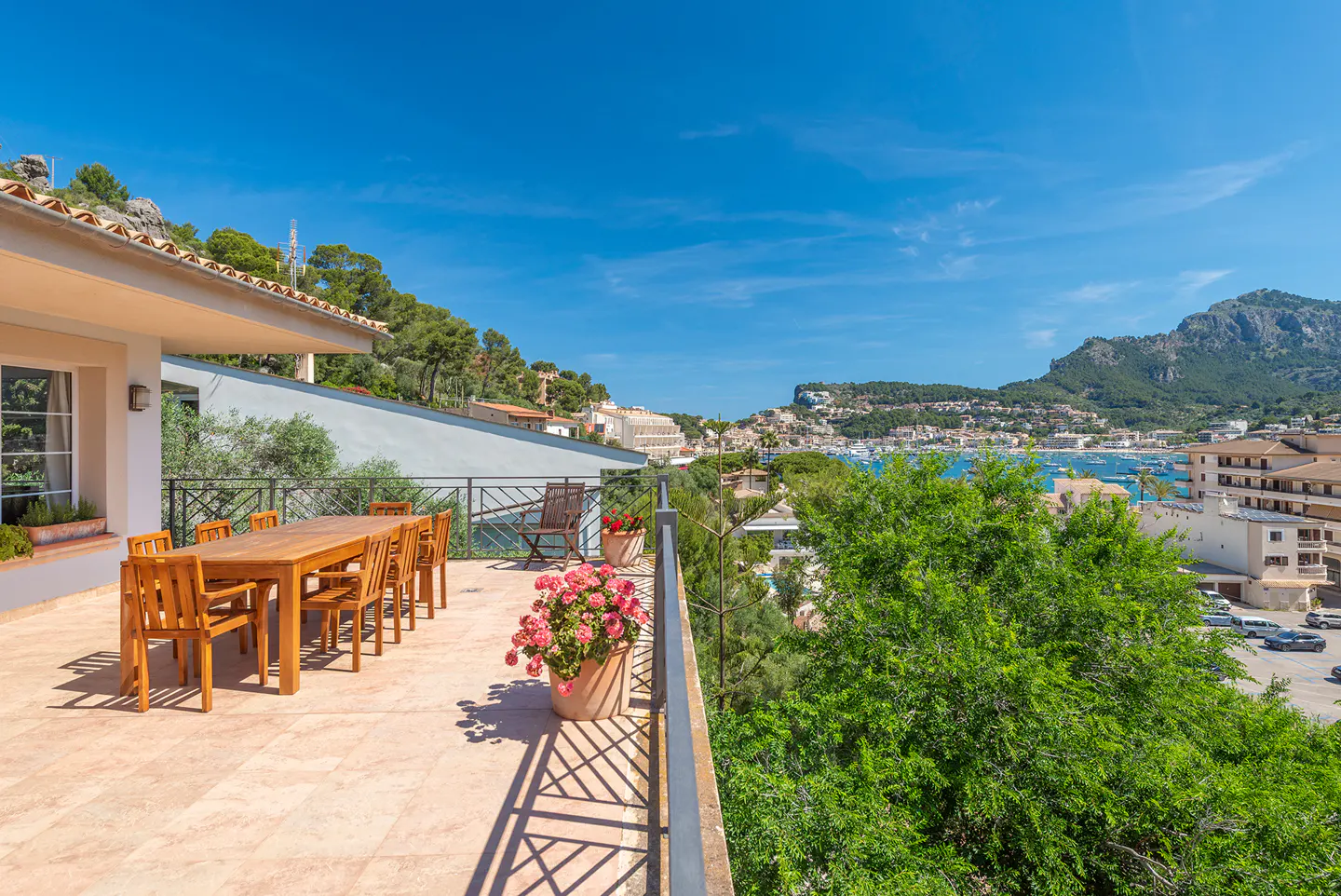 Outdoor patio with a wooden table and chairs overlooking a coastal town and harbor on a sunny day.
