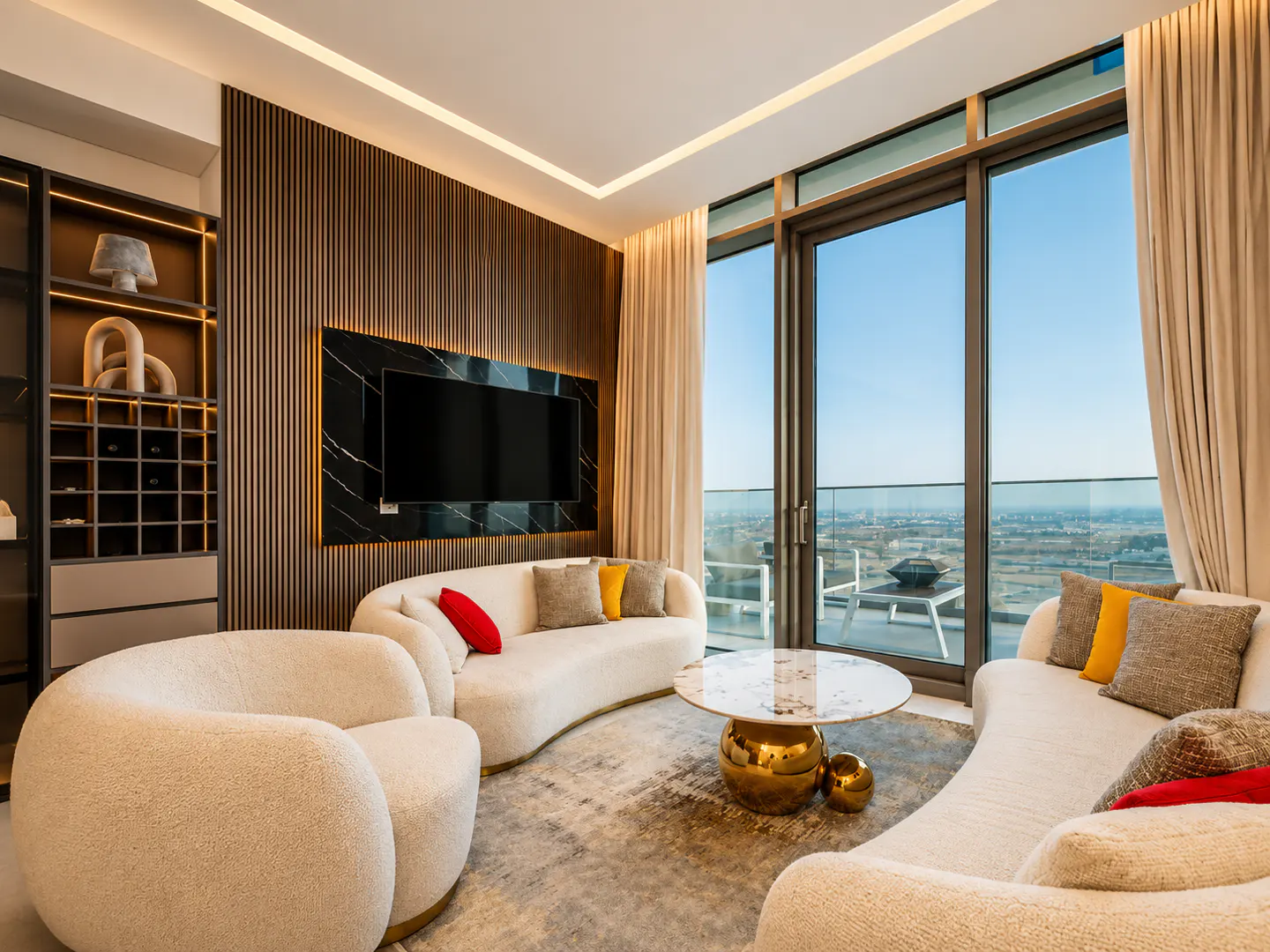 Modern living room with cream curved sofas, a gold-based marble coffee table, and a black marble TV wall with wood slats.