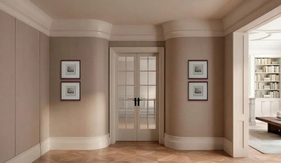 Hallway with beige walls, white trim, and herringbone wood floors. Two framed prints hang on each wall. Double doors lead to another room with a bookcase.