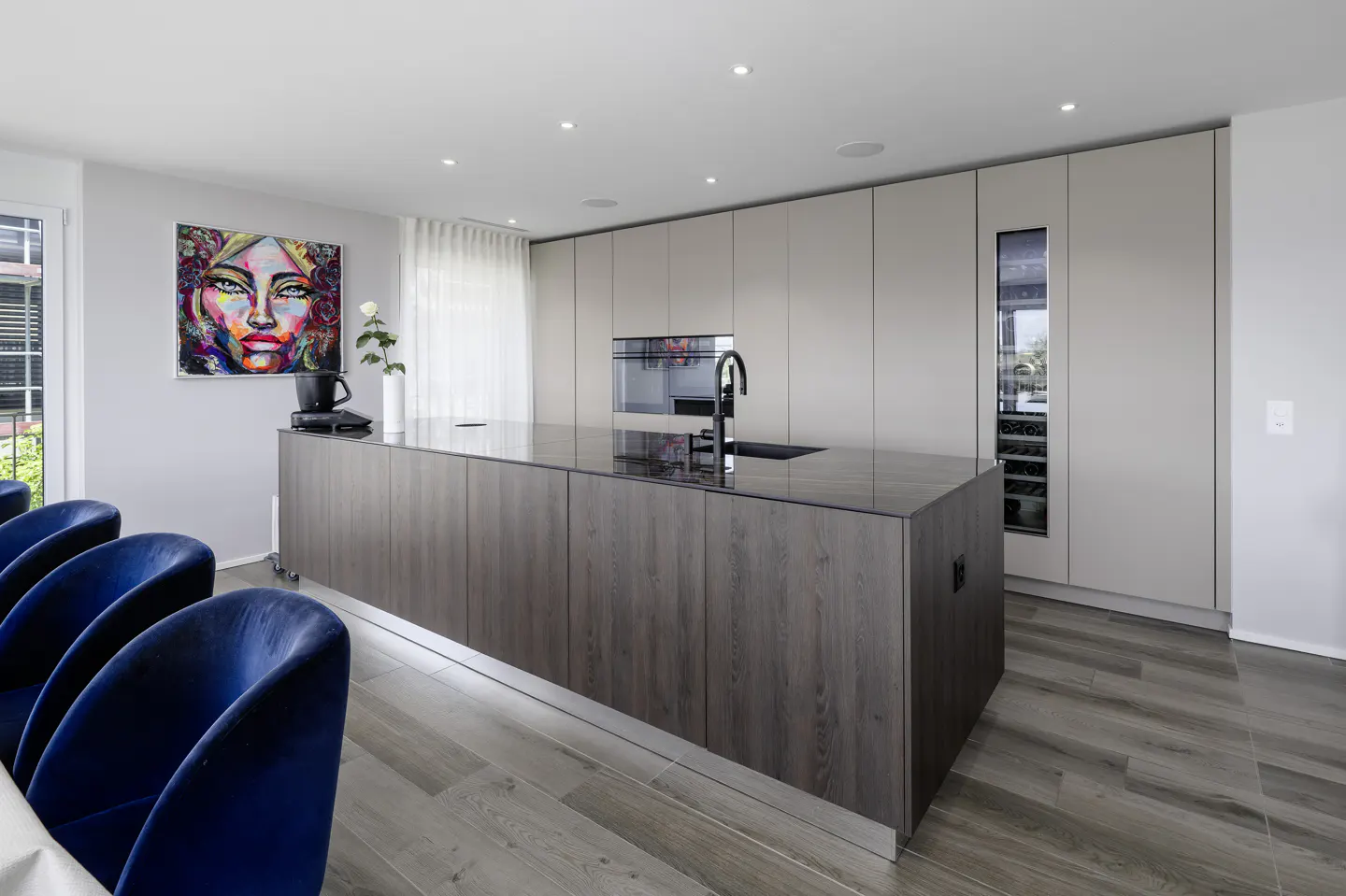 Modern kitchen with a dark wood island, beige cabinetry, built-in wine fridge, and vibrant abstract art on the wall.