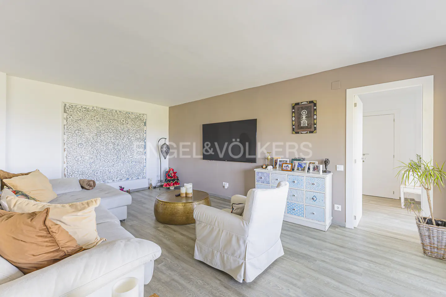 Living room with white sofa, armchair, and gold coffee table on gray wood floors. A TV hangs above a blue and white dresser.
