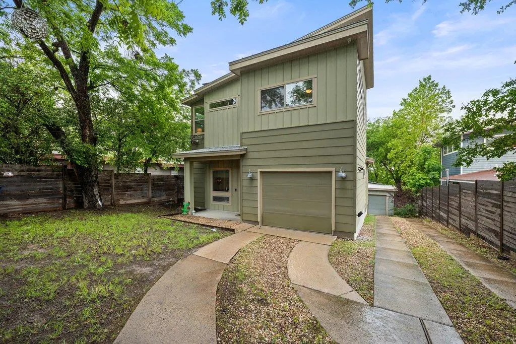 Two-story, green house with a garage and a concrete driveway. Trees and a wooden fence surround the property.