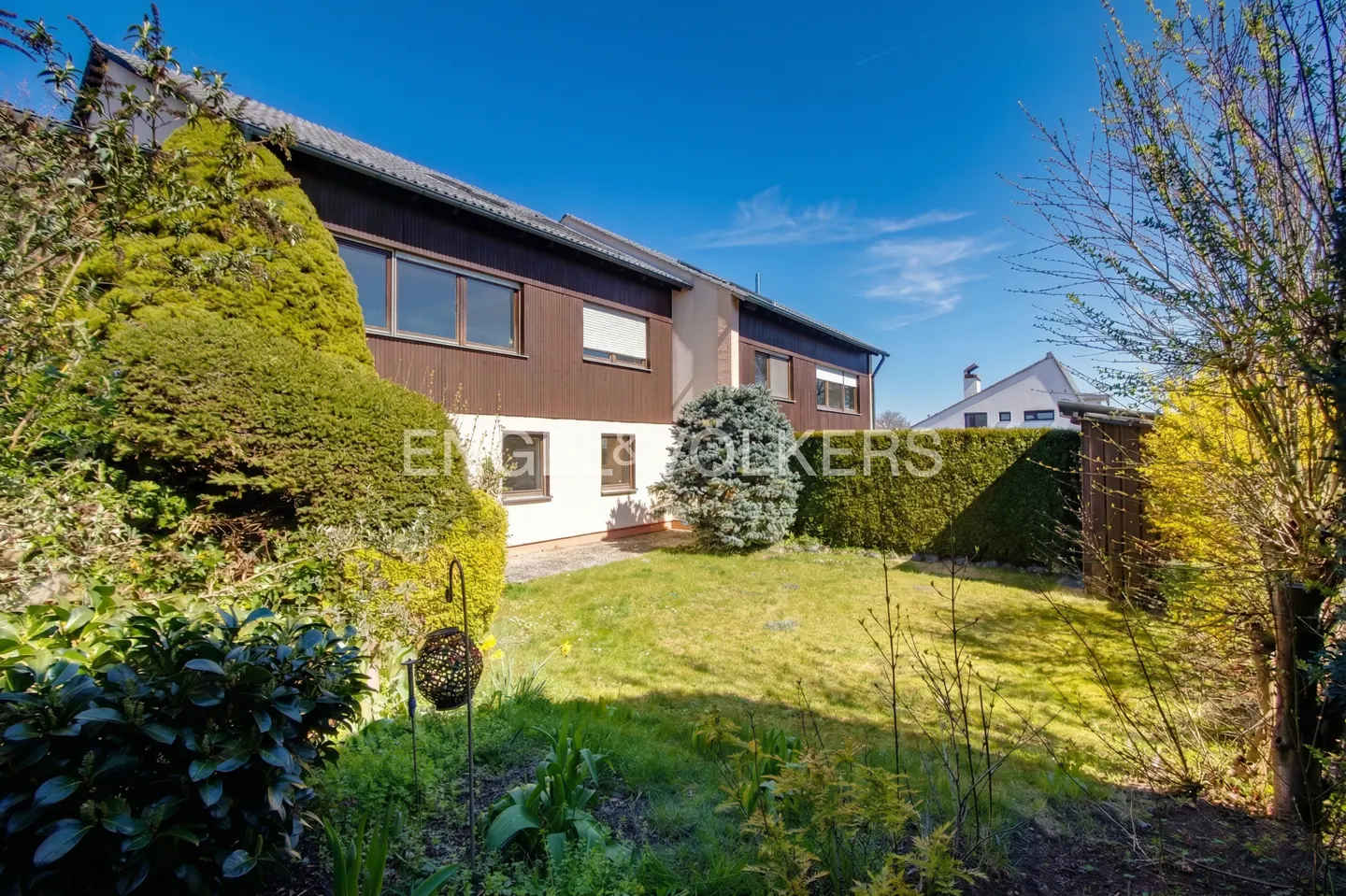 Exterior view of a two-story house with brown siding, white trim, and a green lawn under a blue sky.