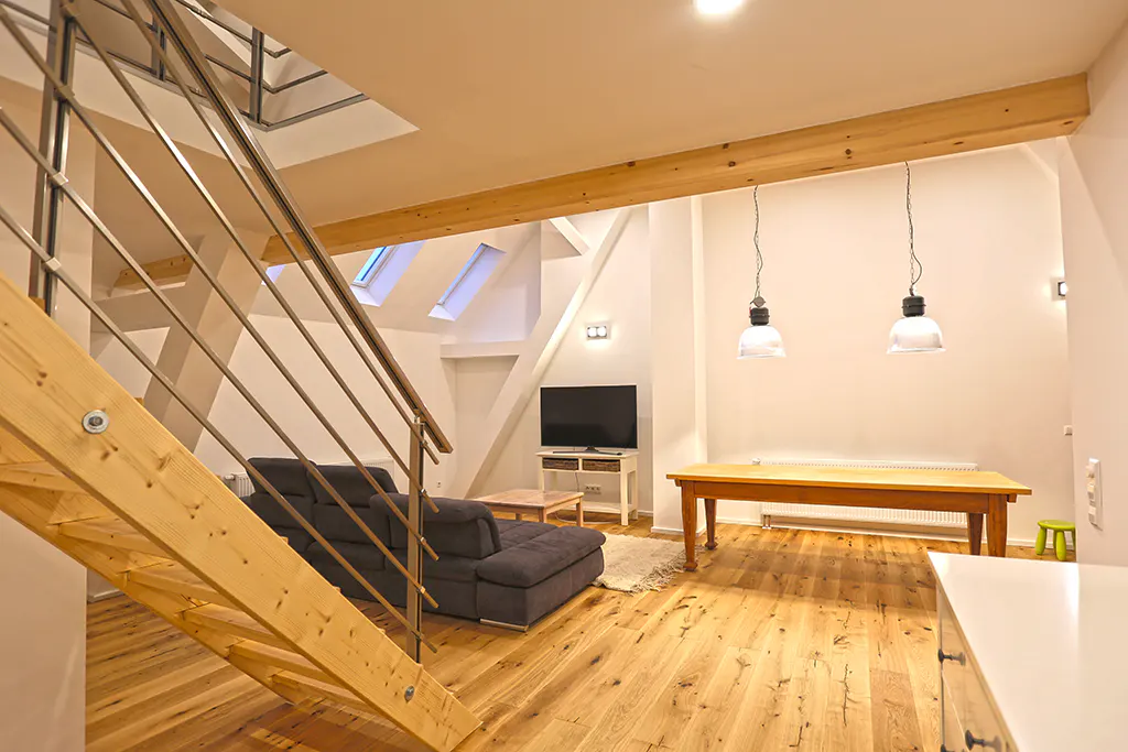 Interior view of a modern living space with wooden floors, a gray sofa, a wooden table, and a staircase with metal railings.