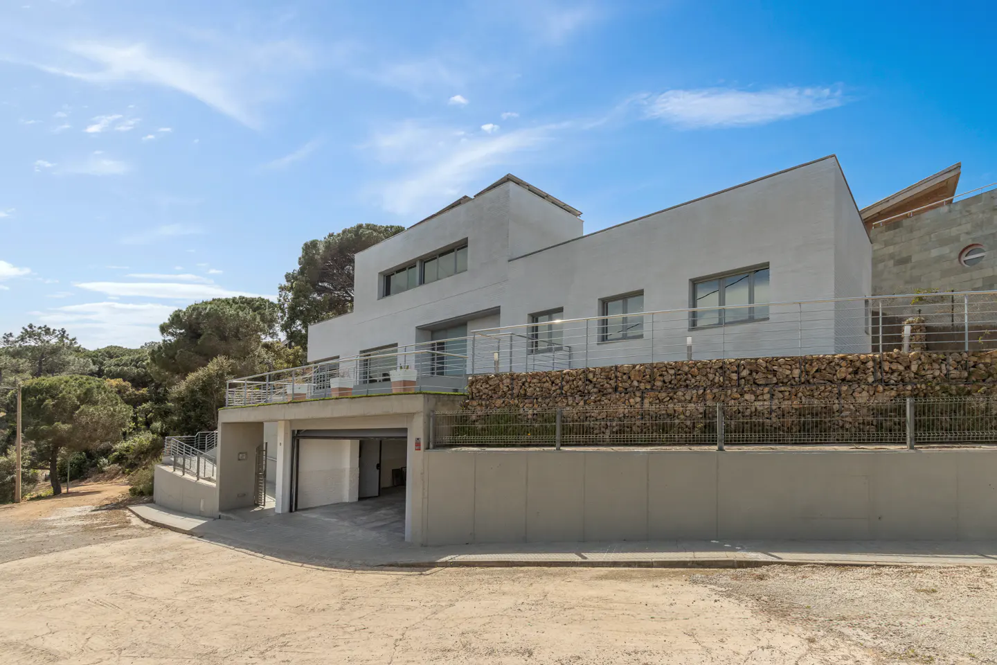 Modern white two-story house with a garage entrance, surrounded by trees and a blue sky.