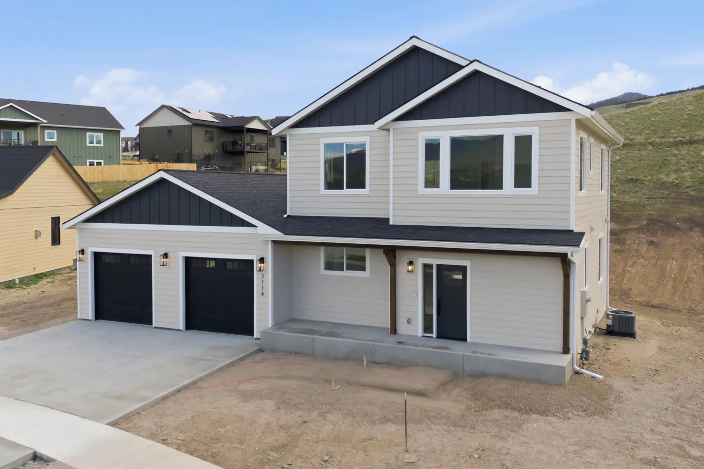 Two-story beige house with a black roof and a three-car garage. A hill is in the background.