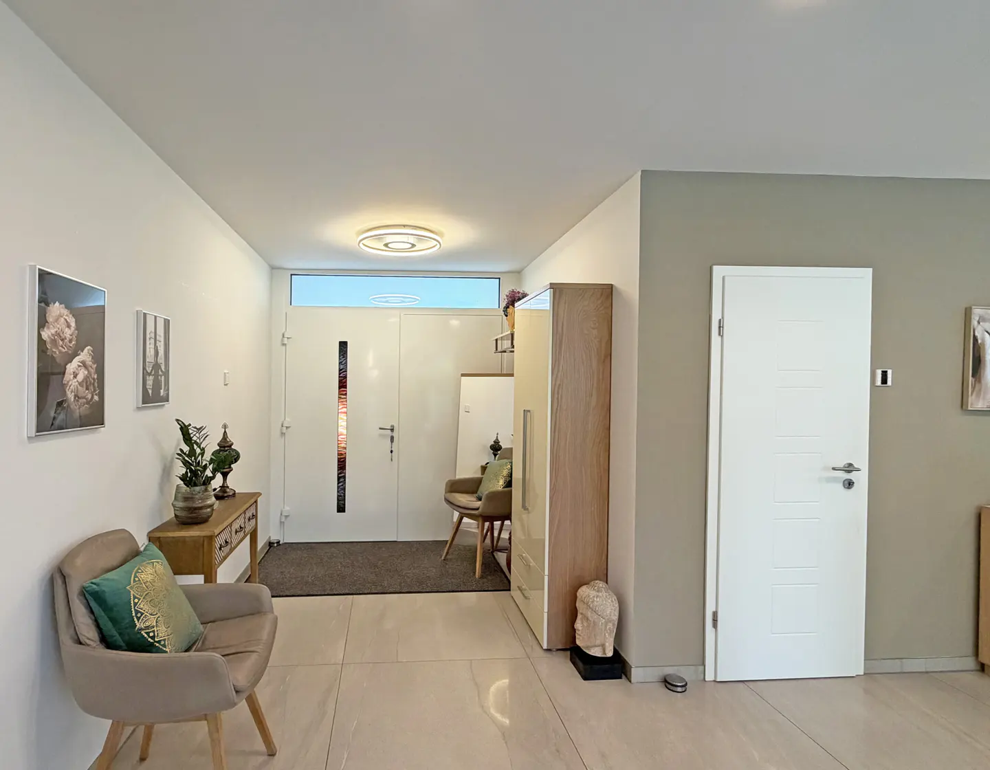 Modern entryway with white door, beige tile floors, a tan armchair with a green pillow, and a wooden console table.