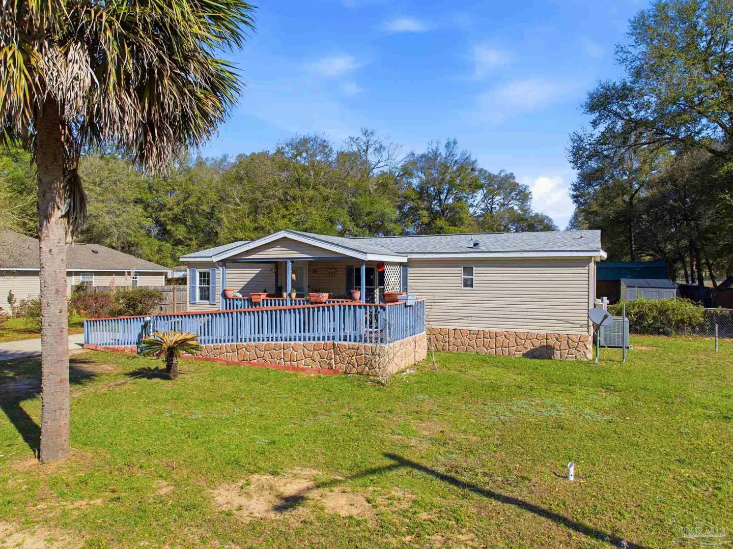 Tan single-story home with a blue deck and stone foundation on a green lawn under a blue sky.