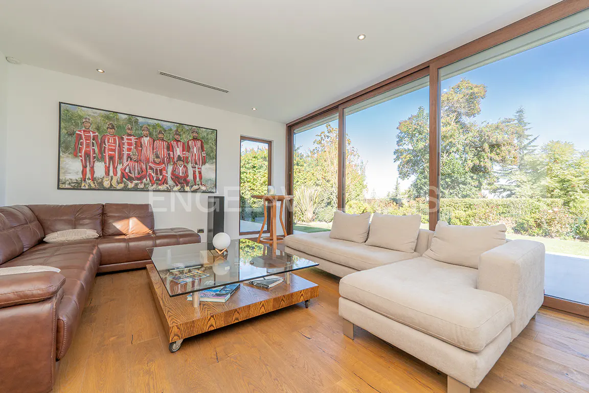 A bright living room with a brown leather sofa, a beige sofa, a glass coffee table, and a large painting on the wall.