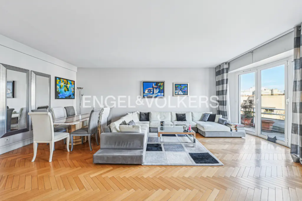 Bright living room with hardwood floors, a white sectional sofa, and a dining table with chairs. Balcony with city views.