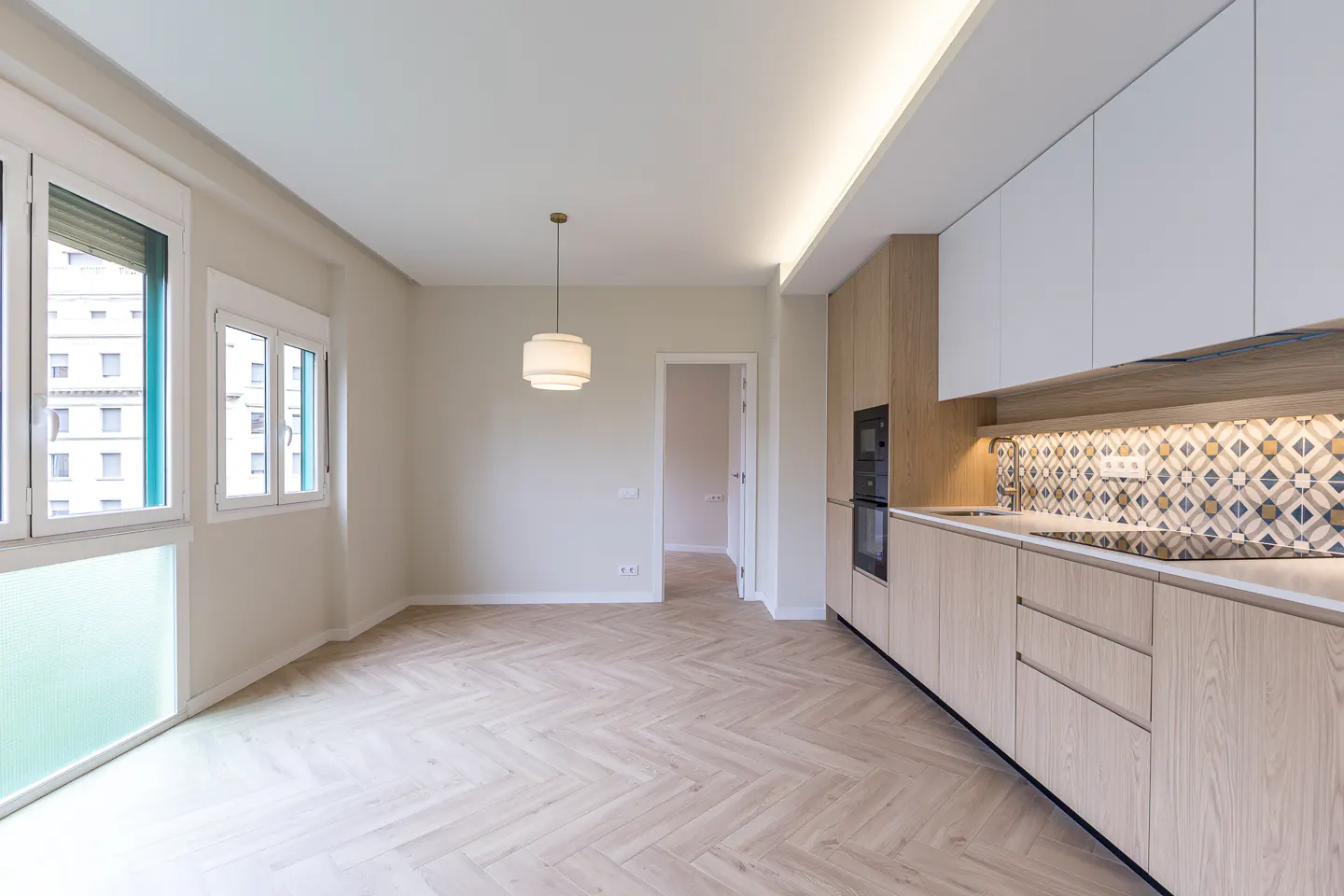 Modern kitchen with light wood cabinets, white upper cupboards, patterned backsplash, and herringbone wood flooring.