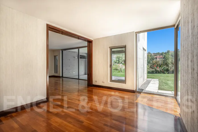 An interior view of a room with hardwood floors, a window, and a doorway leading to a garden.