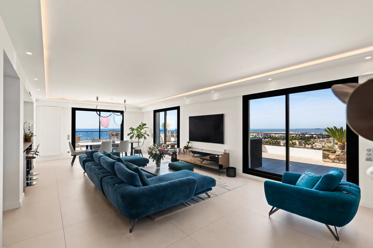 Modern living room with blue velvet sofa and armchair, large windows, and a scenic ocean view from the balcony.