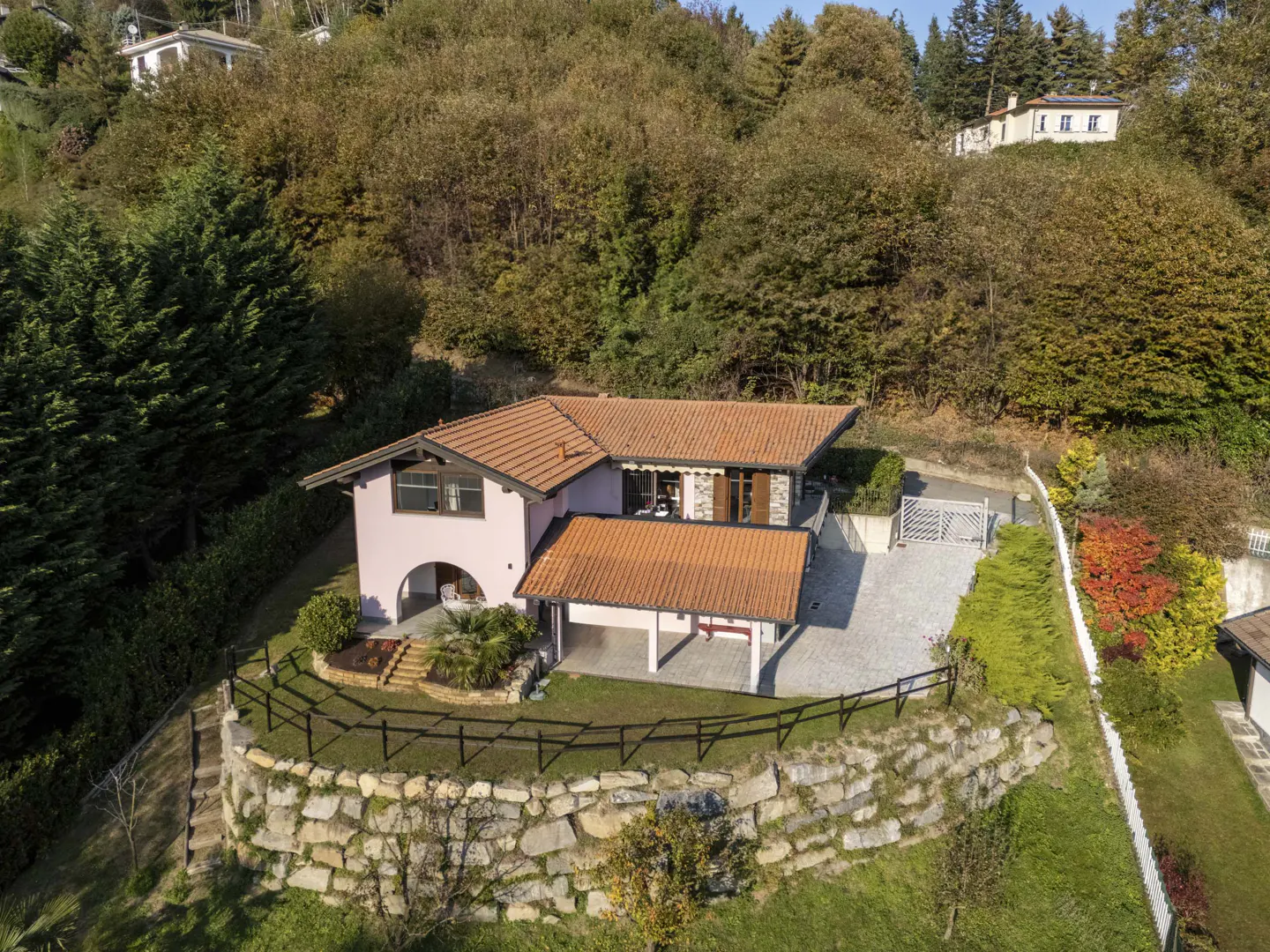 Aerial view of a pink house with a terracotta roof, surrounded by trees and a stone wall.