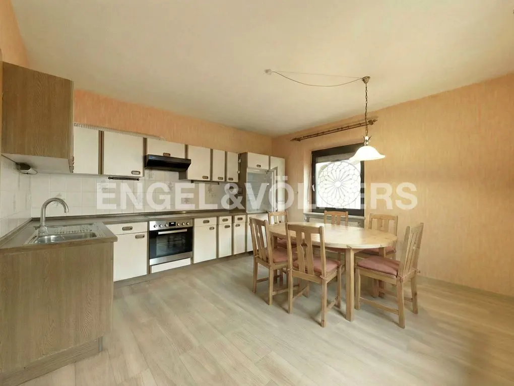 A kitchen with white cabinets, stainless steel appliances, and a round wooden table with six chairs. The walls are peach-colored.