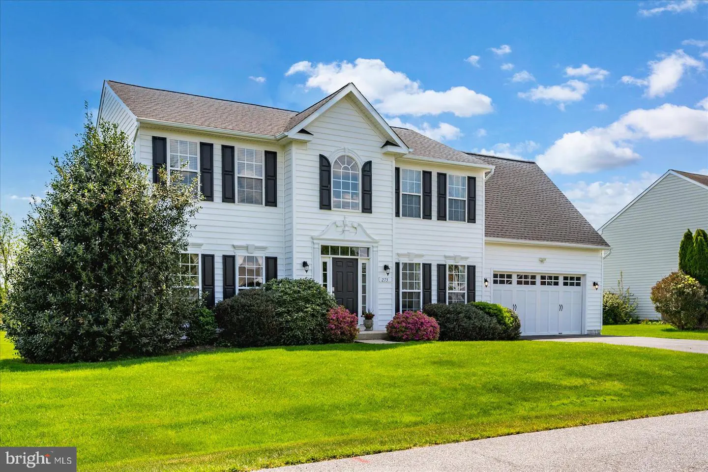 Two-story white house with black shutters, a gray roof, and a two-car garage on a green lawn under a blue sky.